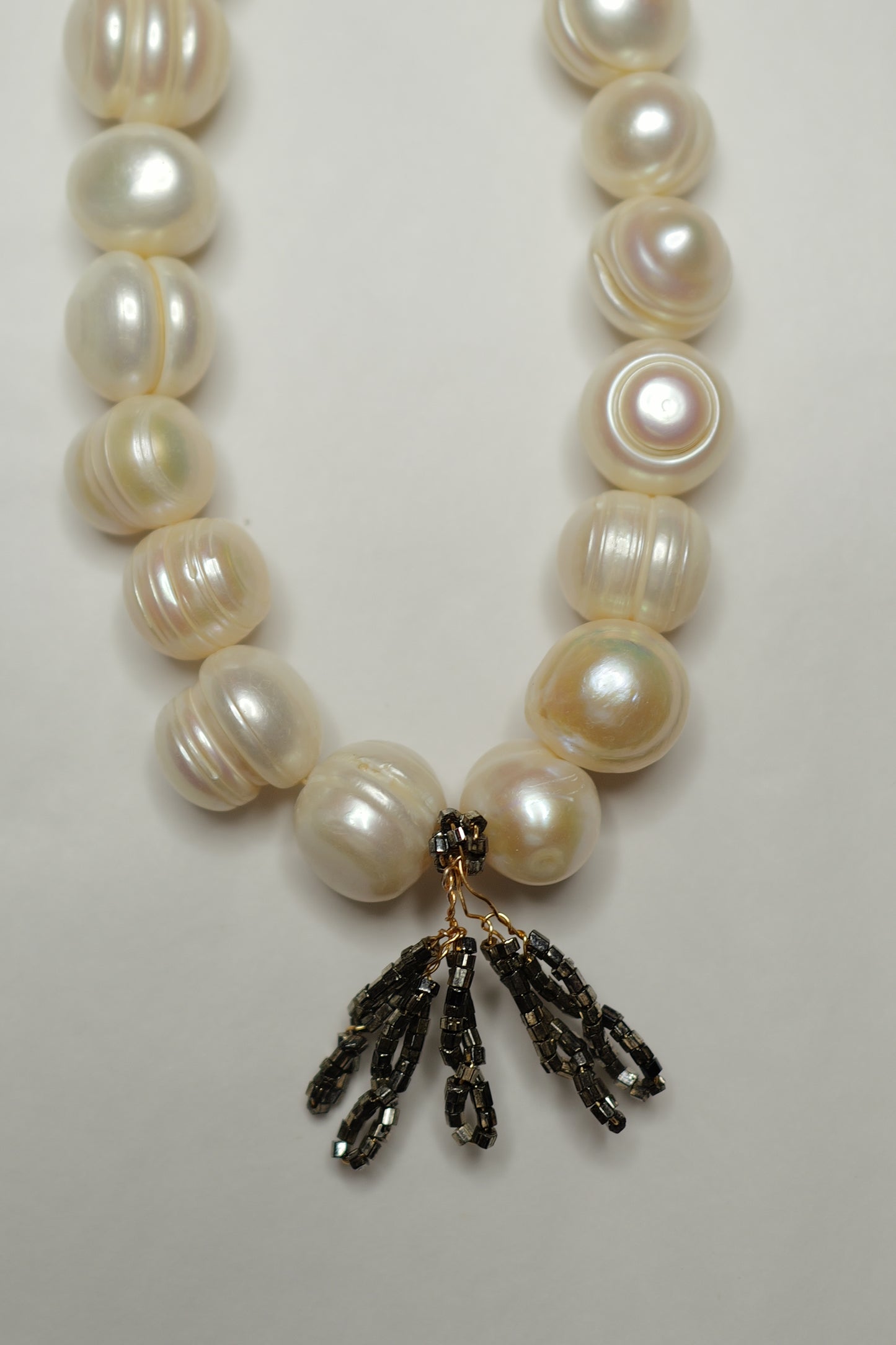 Pearl necklace with a black and gold clasp on a light background