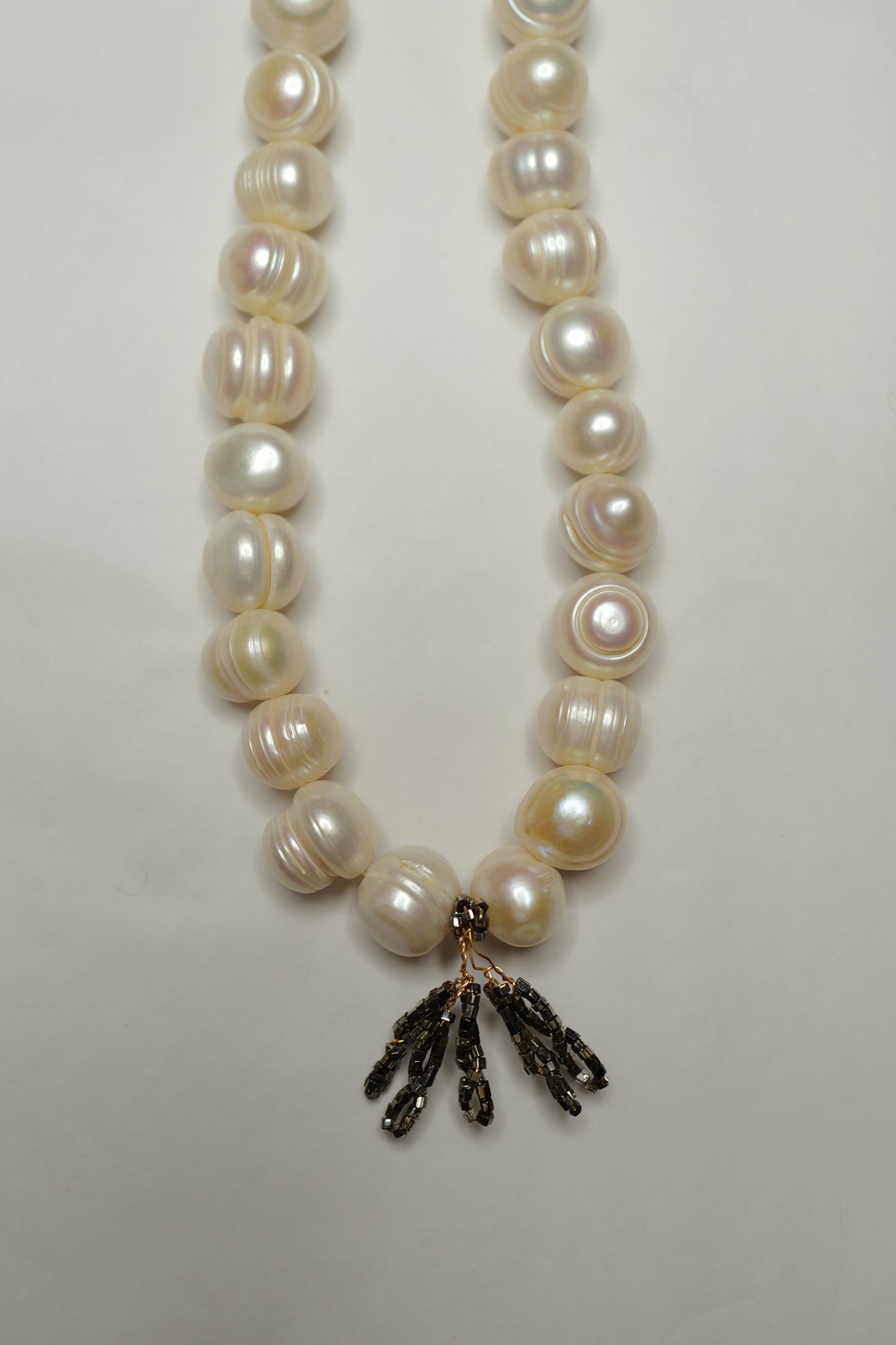 Pearl necklace with a black floral pendant on a light gray background