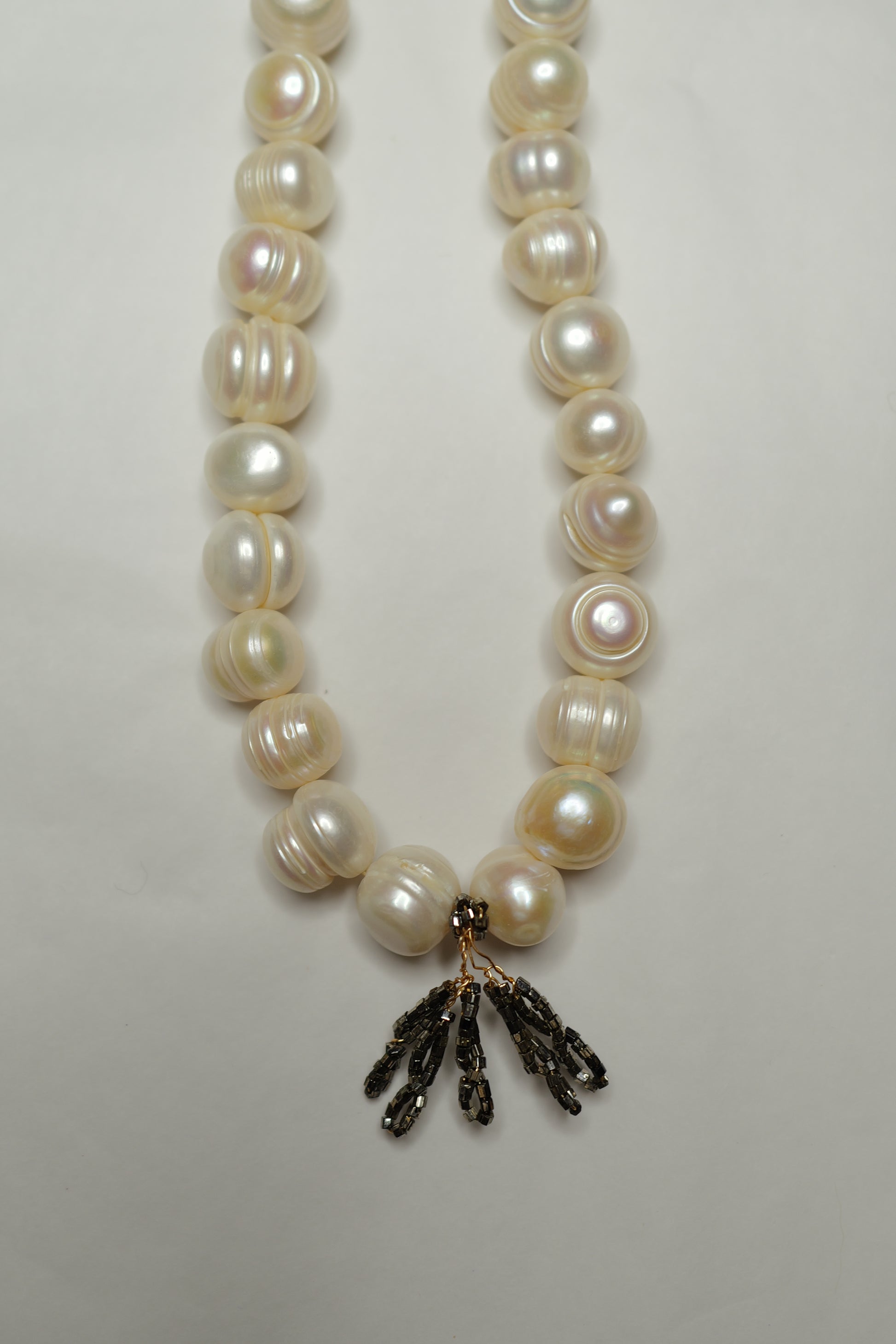 Pearl necklace with a black floral pendant on a light gray background